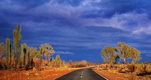 Dark storm clouds gather over Australia's Lasseter Highway as it winds through the red sand desert -- Theo Allofs/CORBIS &copy; (Bing New Zealand)