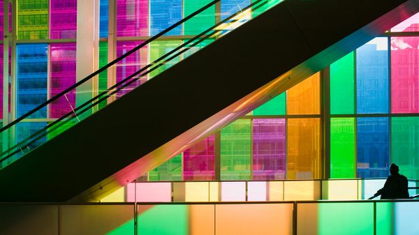 Silhouetted man standing in front of multi-coloured glass windows of Montreal's Palais des Congres Montreal, Quebec, Canada