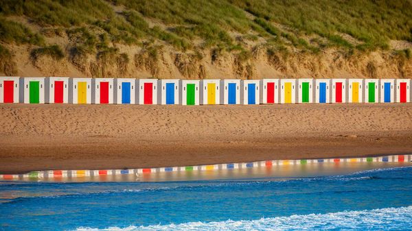 Beach huts reflecting in the water at Woolacombe Beach, Devon