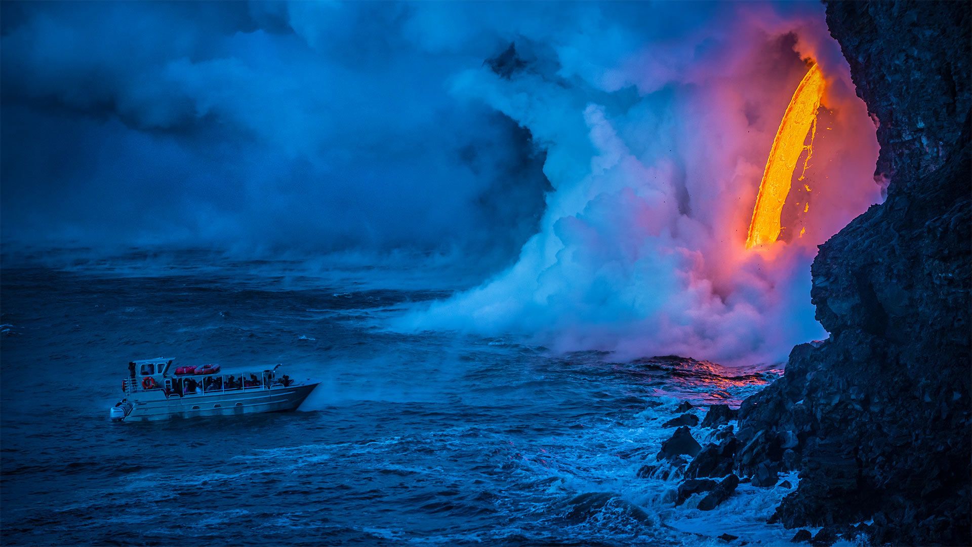 A lava flow hits water to create an explosion as a tourist boat passes, Hawaii Volcanoes National Park, USA