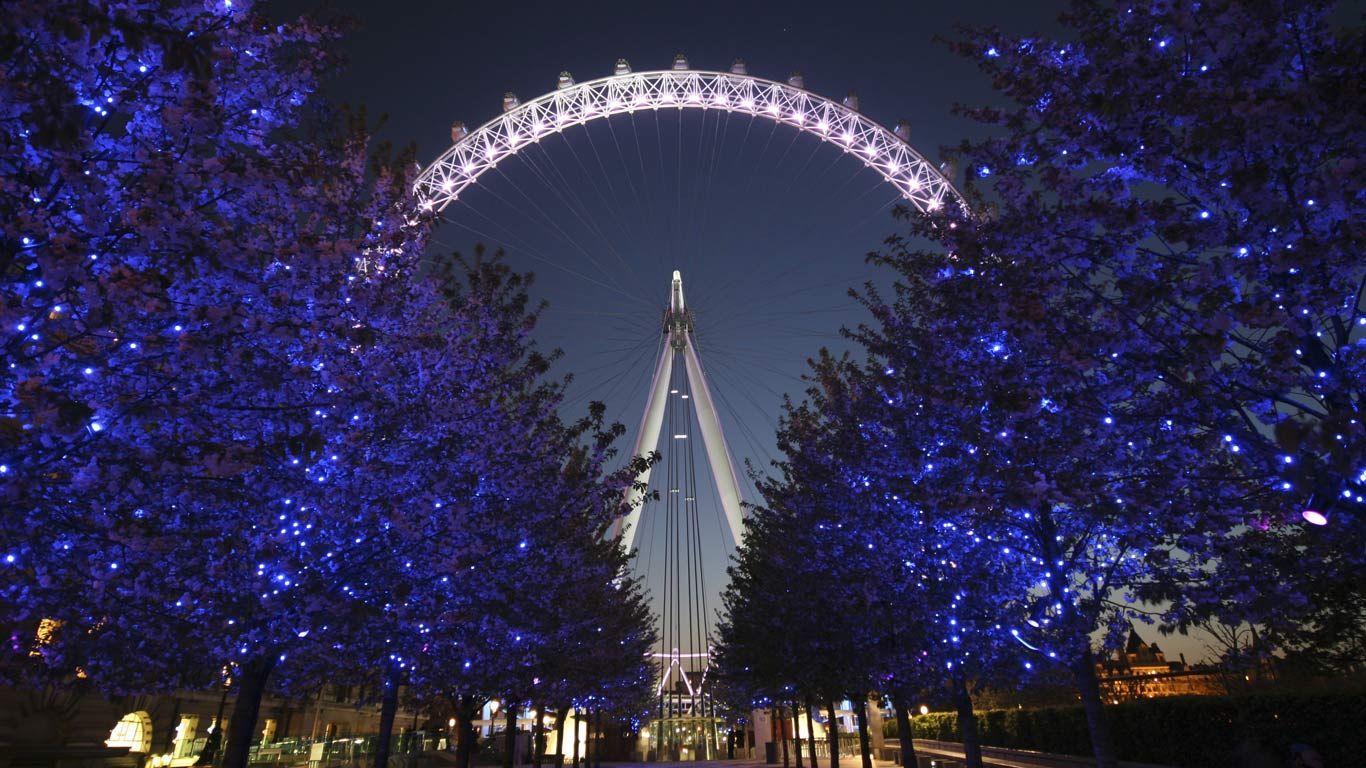 The London Eye at night behind illuminated trees