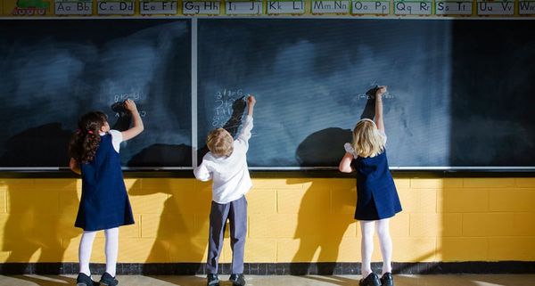 Three students writing on blackboard in classroom