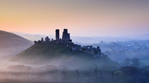 Corfe Castle shrouded in mist at sunrise in Dorset, England