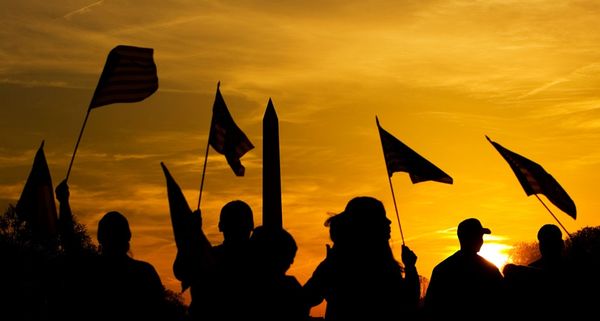 People holding American flags at sunset near the Washington Monument in Washington, D.C.