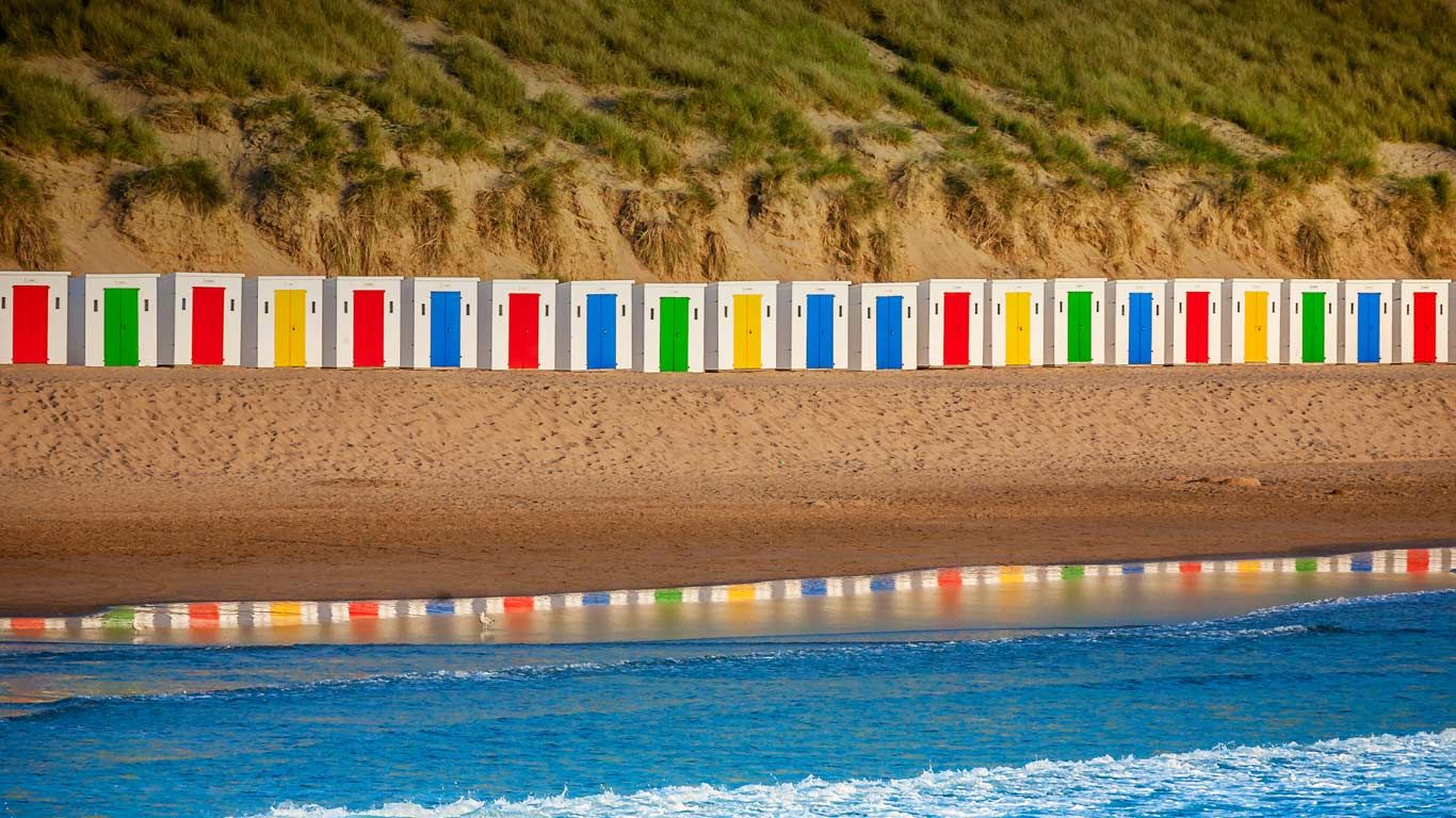 Beach huts reflecting in the water at Woolacombe Beach, Devon, England
