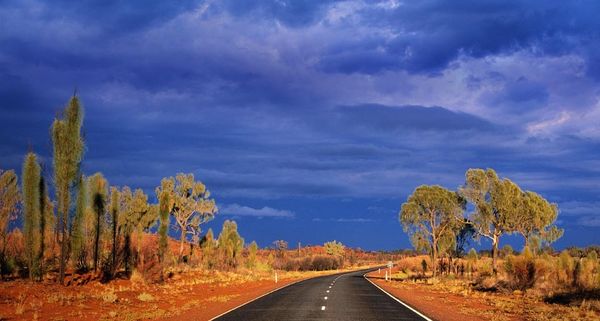 Dark storm clouds gather over Australia's Lasseter Highway as it winds through the red sand desert