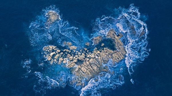 Ocean waves crashing over a heart-shaped rock island off the coast of Sydney, Australia