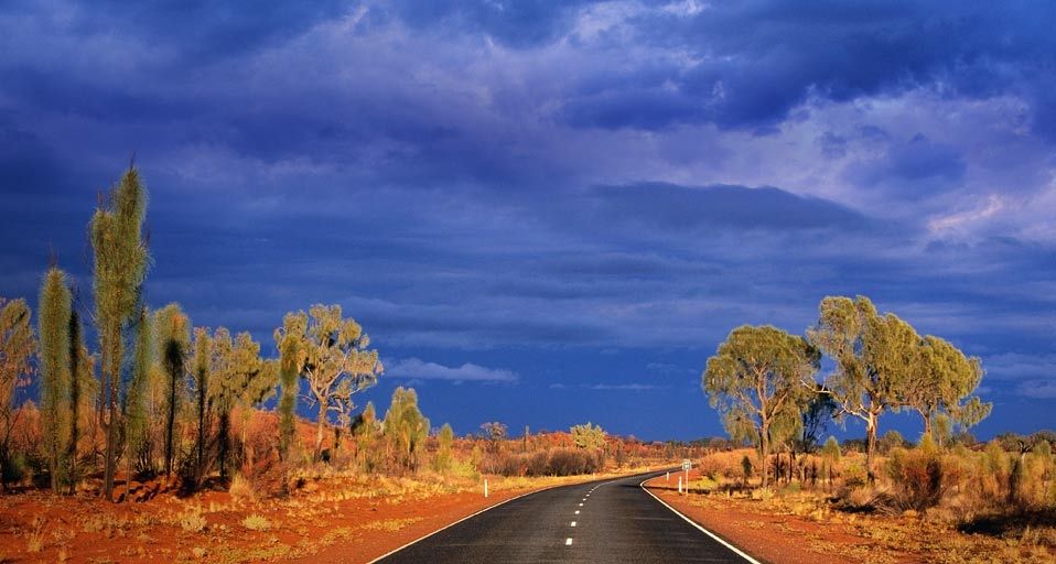 Dark storm clouds gather over Australia's Lasseter Highway as it winds through the red sand desert