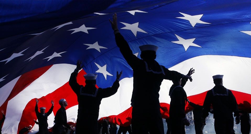 Military personnel stand under a huge American flag preceding a San Diego Chargers football game, San Diego, Calif.