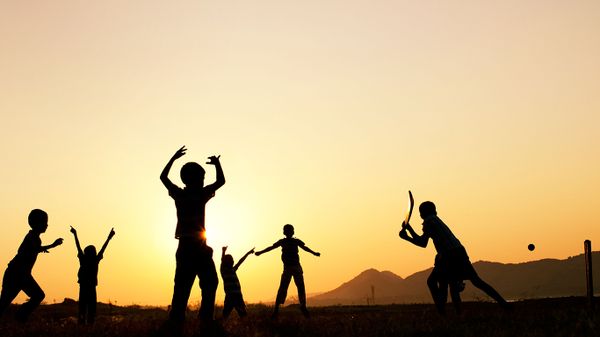 Silhouette of young Indian boys playing cricket against a sunset background