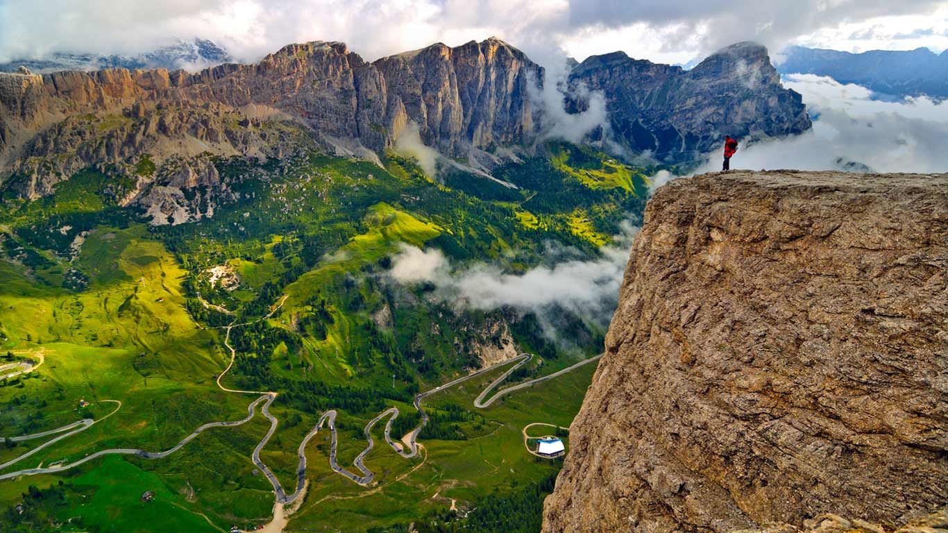 Trekker on the Sella Group mountain chain, looking down on the road from Badia Valley to Gardena Pass, Dolomites, South Tyrol, Italy
