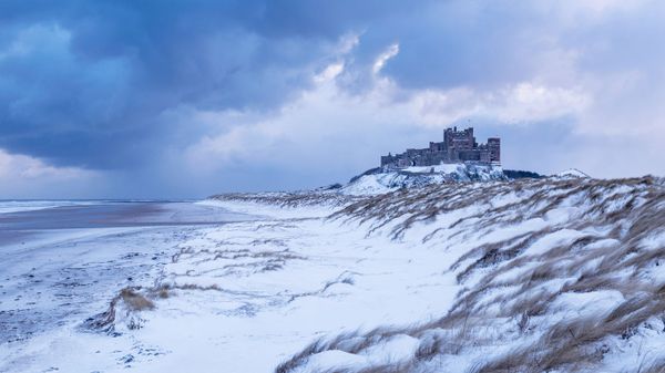 Bamburgh Castle and sand dunes after snowfall in Northumberland