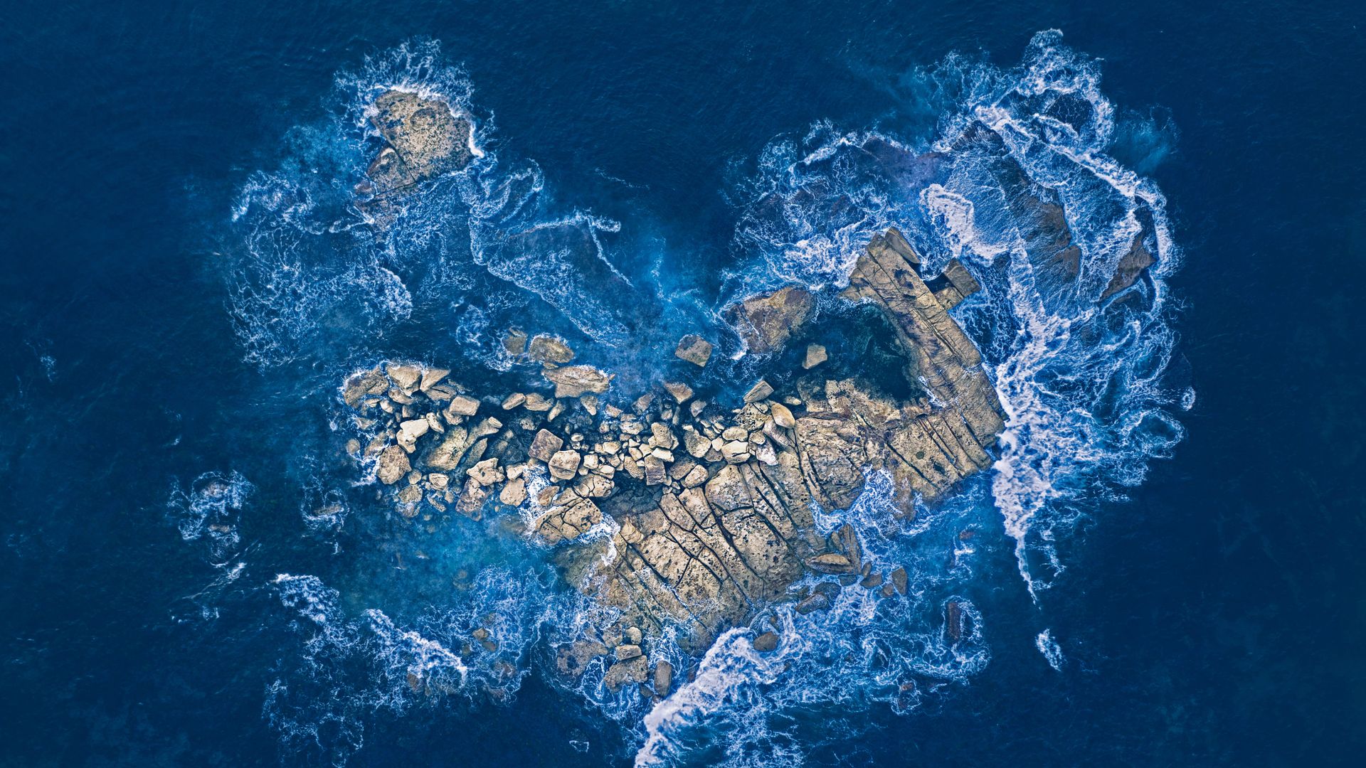 Ocean waves crashing over a heart-shaped rock island off the coast of Sydney, Australia
