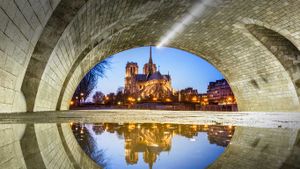 Notre-Dame de Paris se reflétant dans l’eau sous le pont de la Tournelle la nuit, Paris, Île de France (© Loic Lagarde/Getty Images)(Bing France)